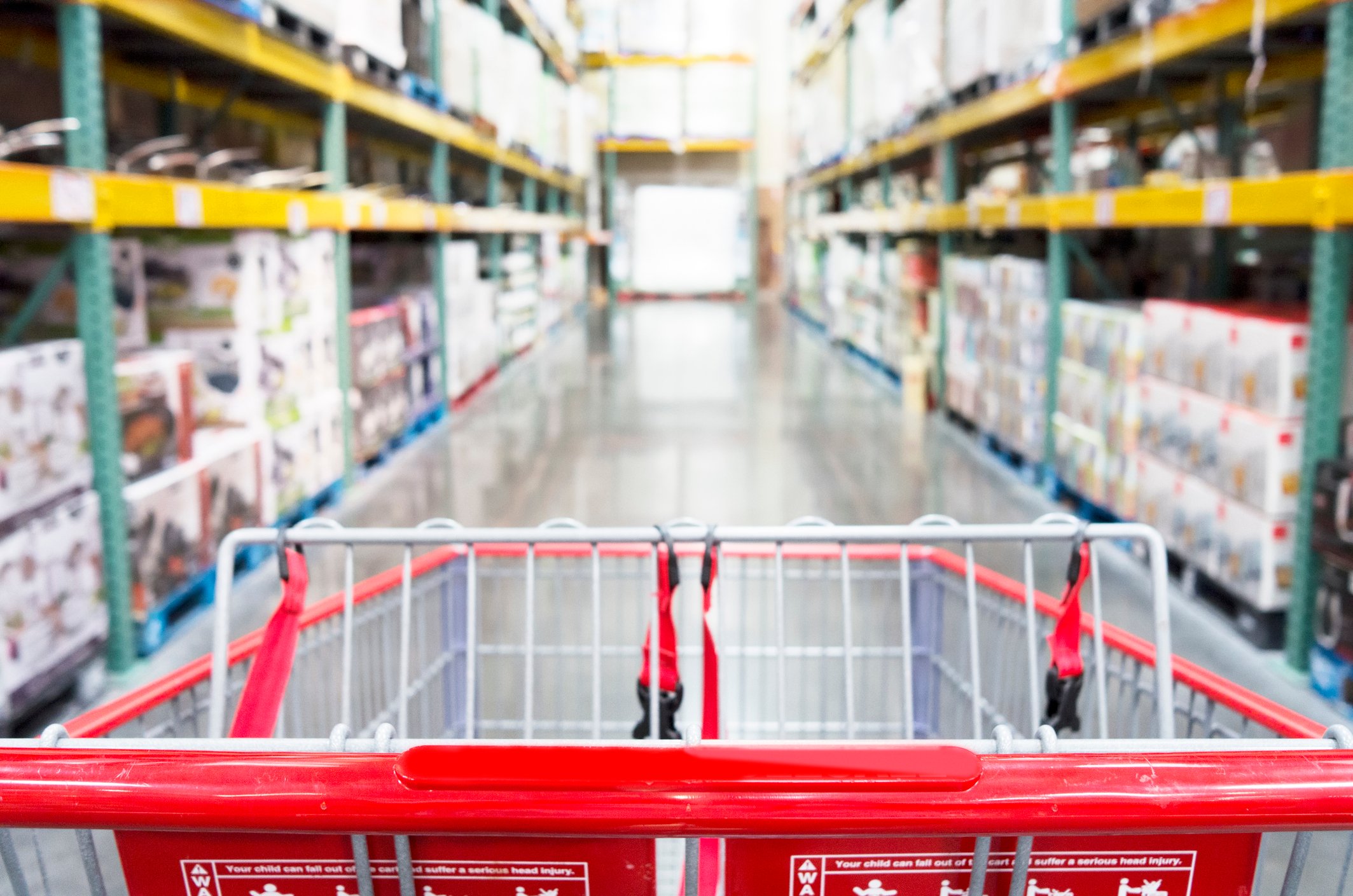A grocery cart in the aisle of a warehouse.