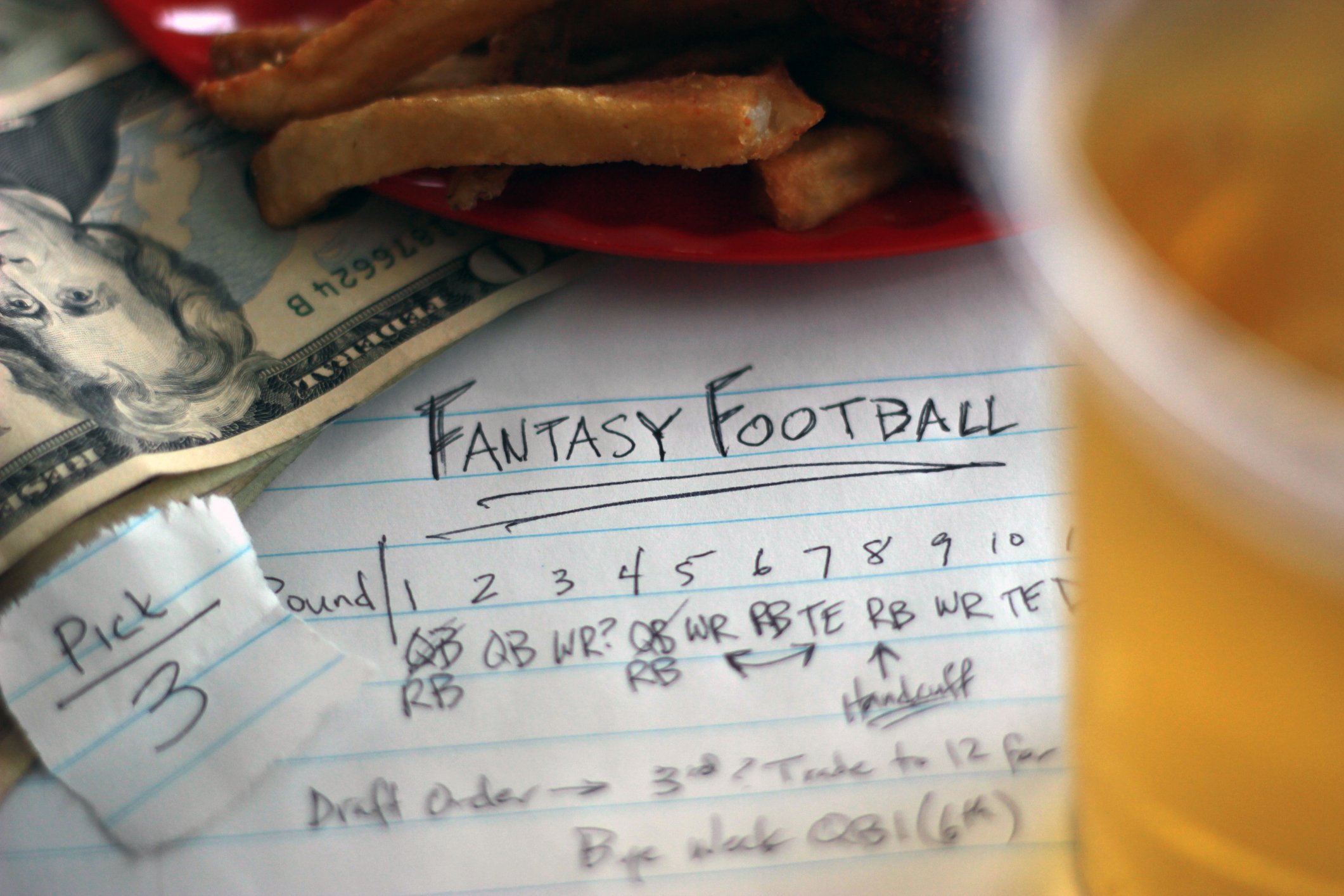 A piece of paper with fantasy football notes, sitting under a plate of french fries and a beer.