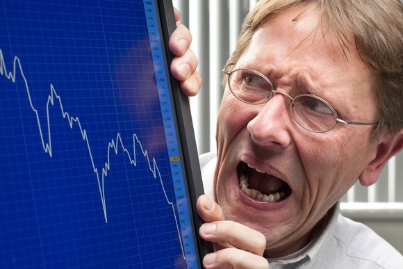 Horrified-looking man viewing falling stock chart on computer