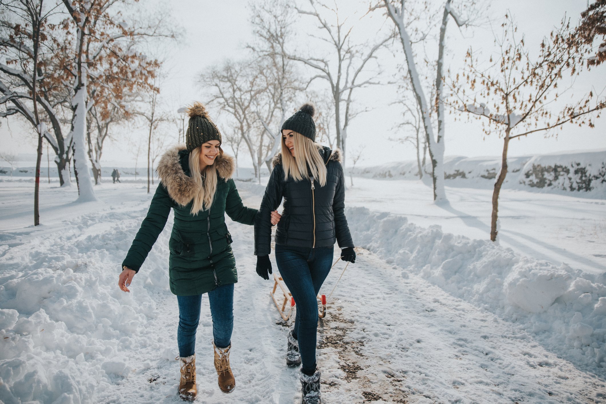 Two women wearing parkas walk down a snowy lane.