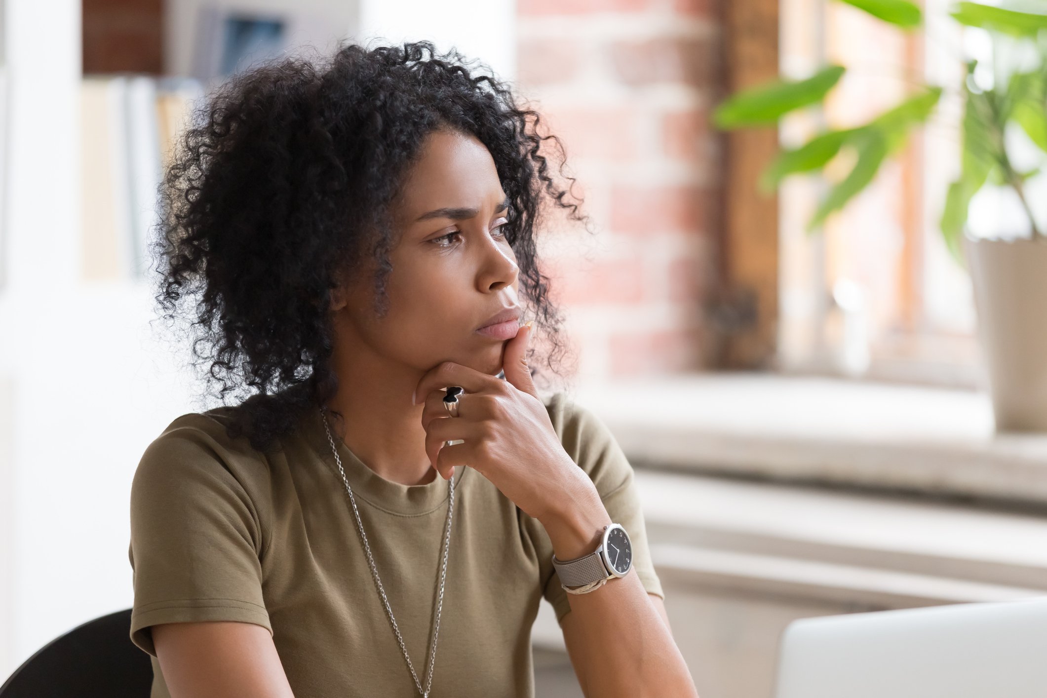 A woman with her hand on her chin looking out the window, pondering a decision. 