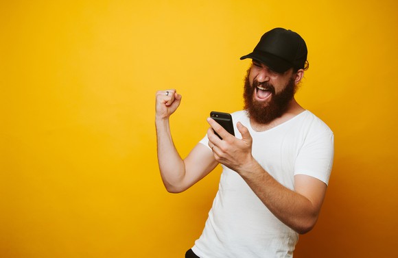 A man looking at his phone, smiling and celebrating