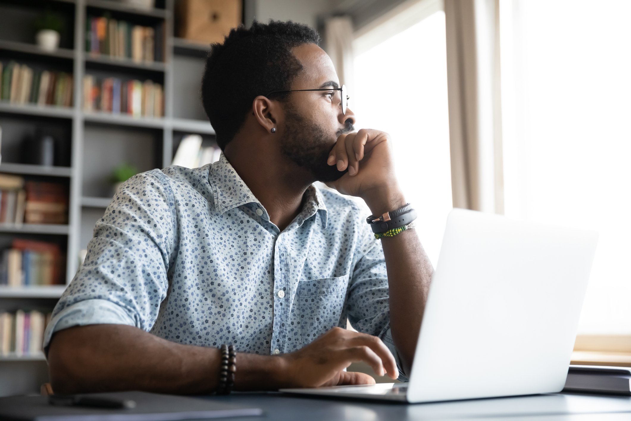 A person sitting at a table on a laptop looking out a window