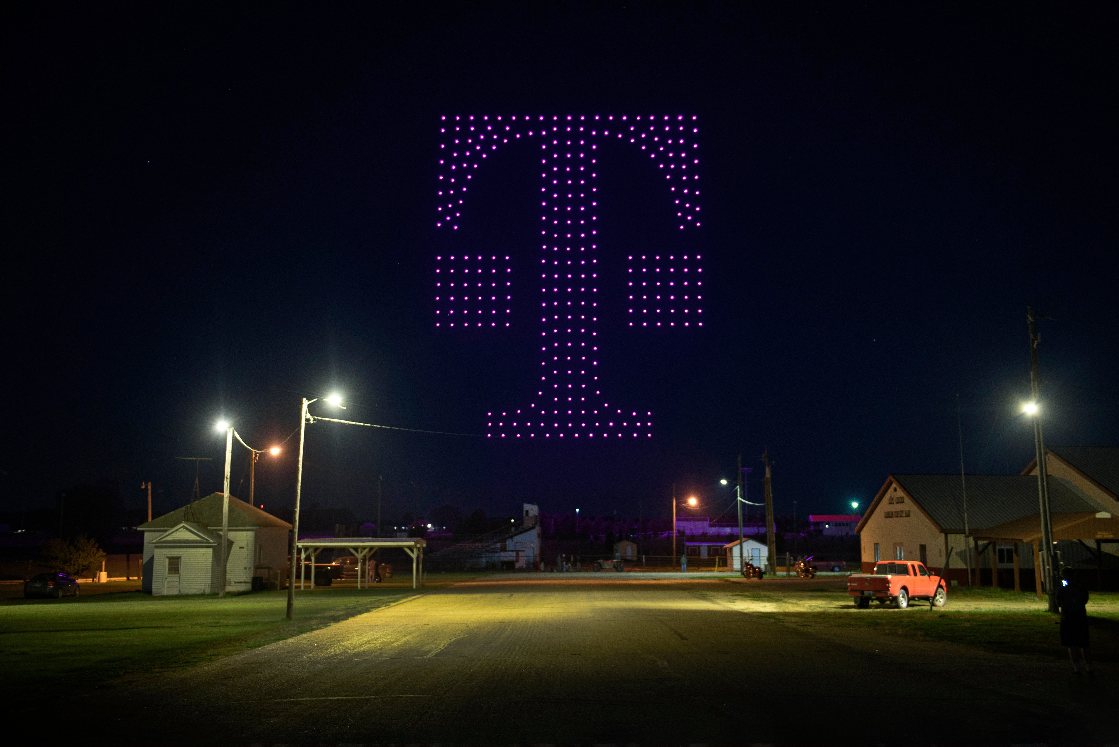 Drones with magenta lights forming the T-Mobile logo in the night sky.