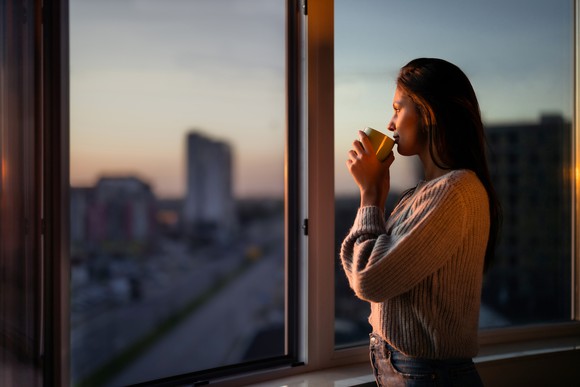 A woman looking out a window while sipping coffee.