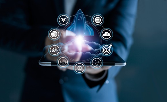 Person holding tablet with digital icon of rocket blasting off above it