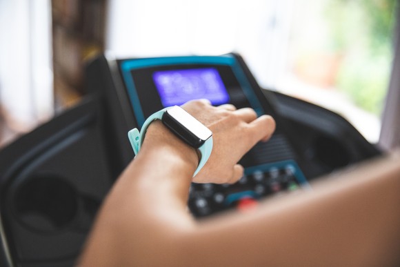 A woman looking at her watch on her wrist while using a treadmill.