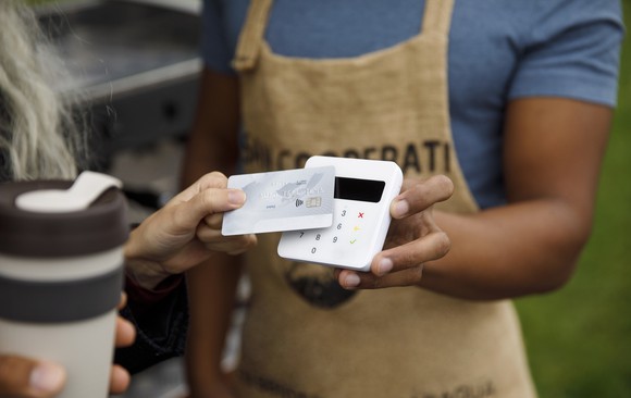 Close-up of a customer tapping a contactless reader with her card in a coffee shop.