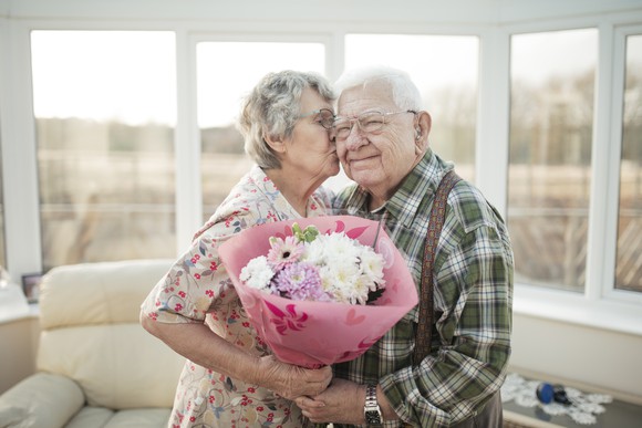 A senior woman receives flowers from her husband and gives him a kiss.