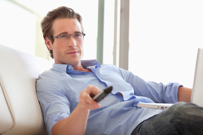 A man watches TV while using a laptop.