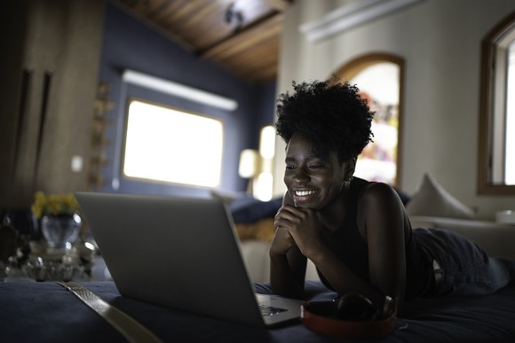 Woman lying on floor on her stomach, watching laptop
