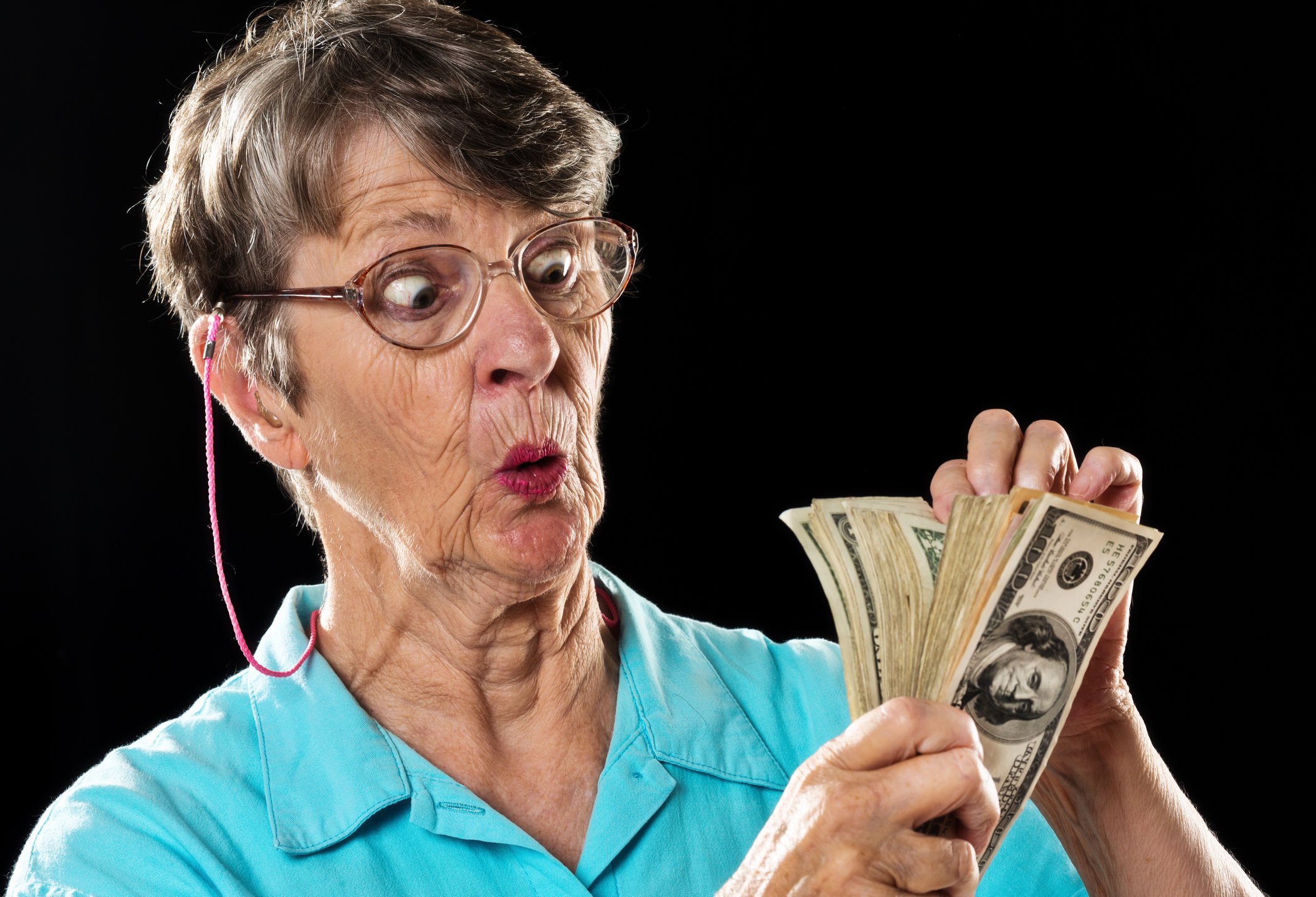 A senior woman is counting a wad of cash and looking impressed.