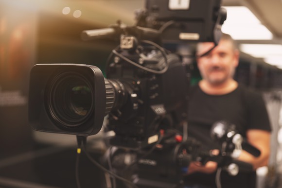 A cameraman sitting behind a TV production camera.