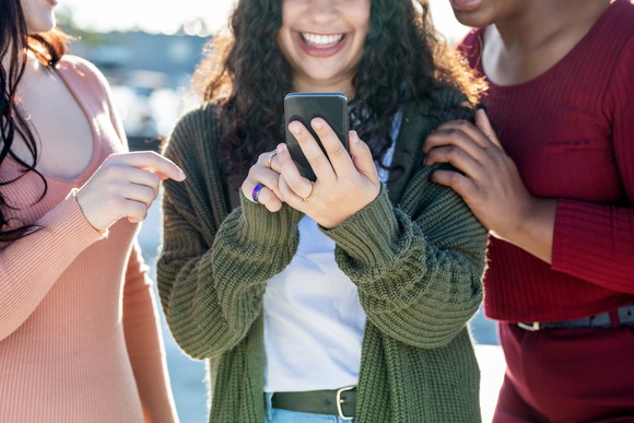 Three young people reacting to something on a smartphone.