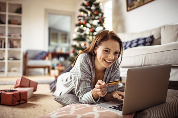 Woman lying on floor with credit card, using laptop