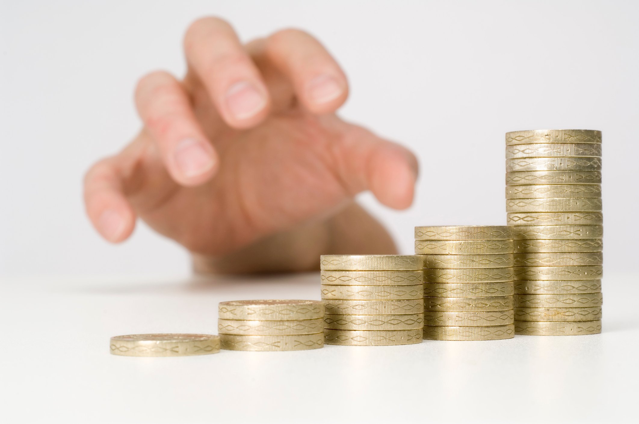 A hand reaches out to take from several stacks of coins.