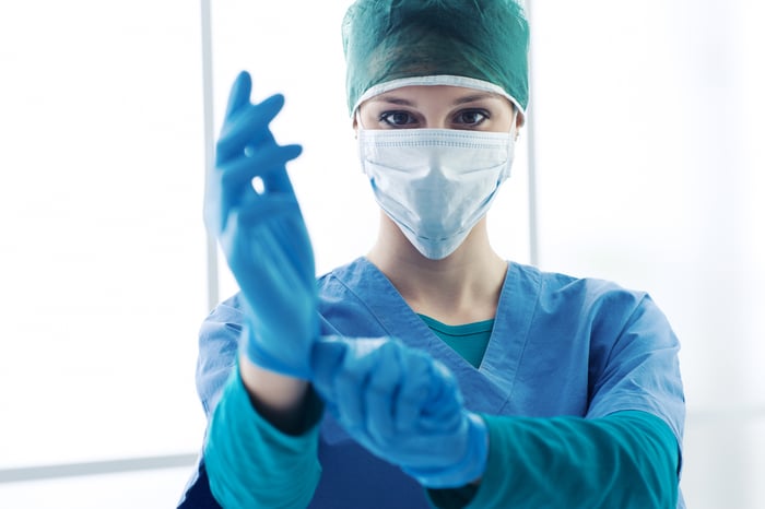 Female surgeon with medical mask puts on a pair of gloves to get ready for surgery.