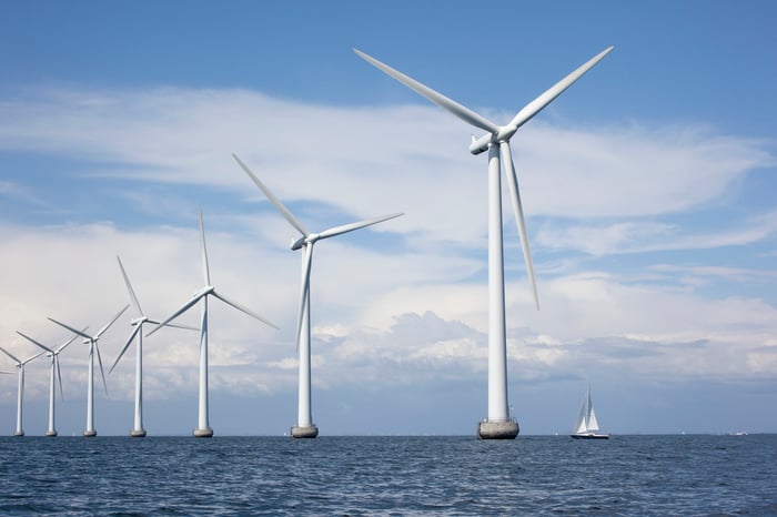 A sailboat passes offshore wind turbines. 