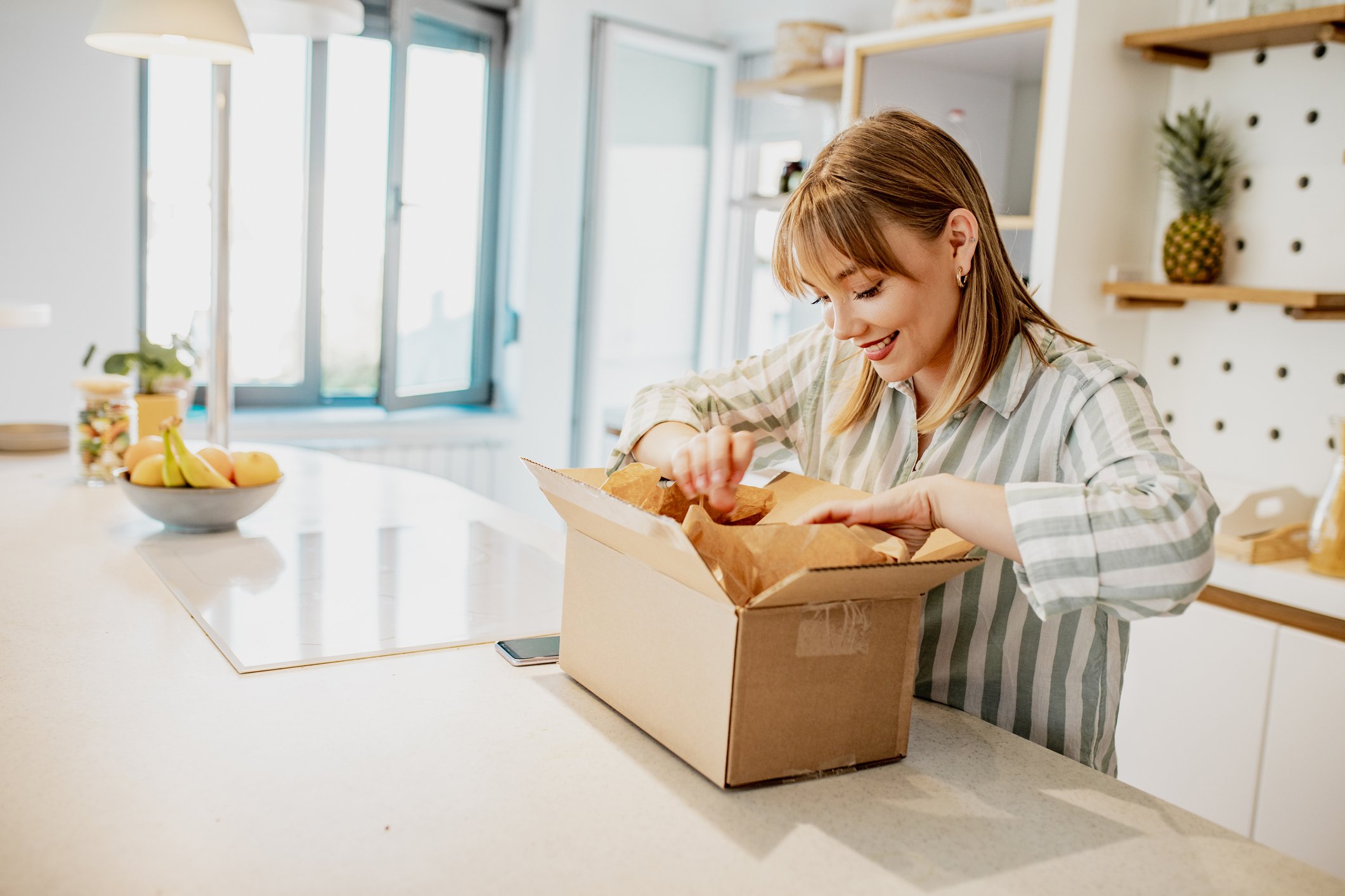 A woman opening a package in her kitchen.
