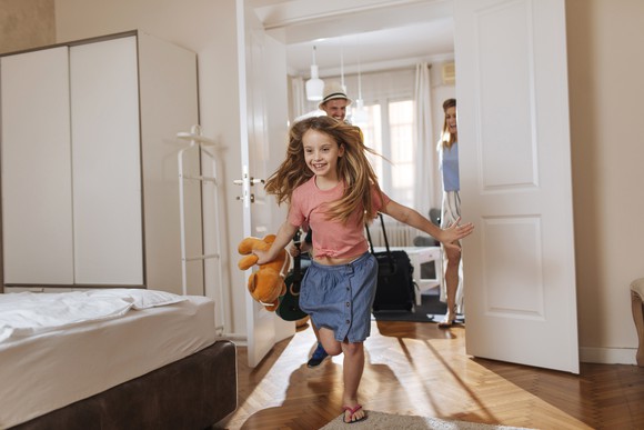 A child running and smiling into a hotel room while her mother and father are watching her in the next room.