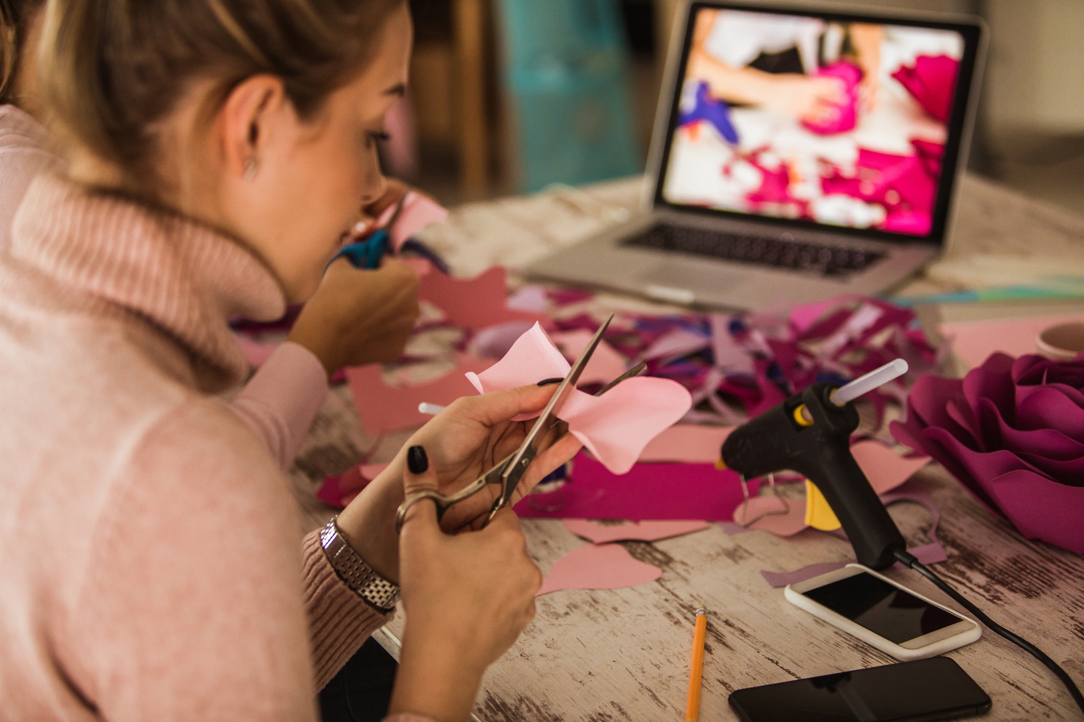 A woman cutting fabric while sitting in front of a laptop