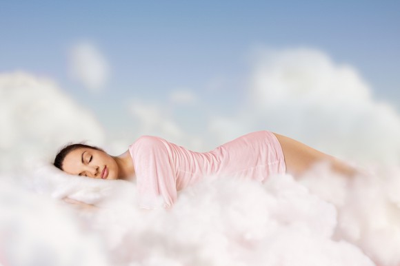 Woman in pink pajamas sleeping in the clouds.