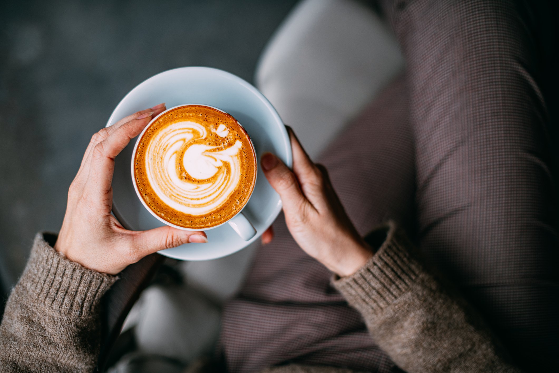 Overhead view of a person's hands holding a mug of latte