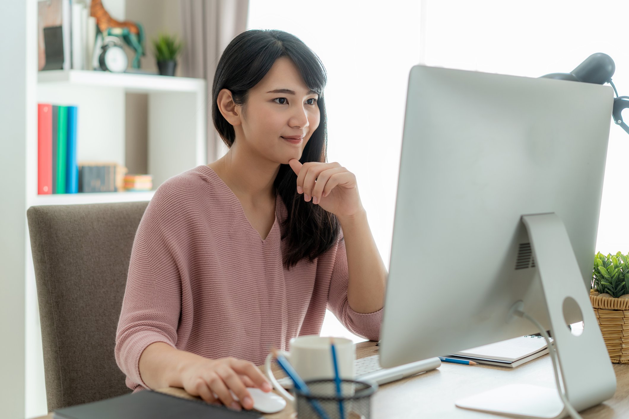 Happy woman seated at a desk, using a PC.