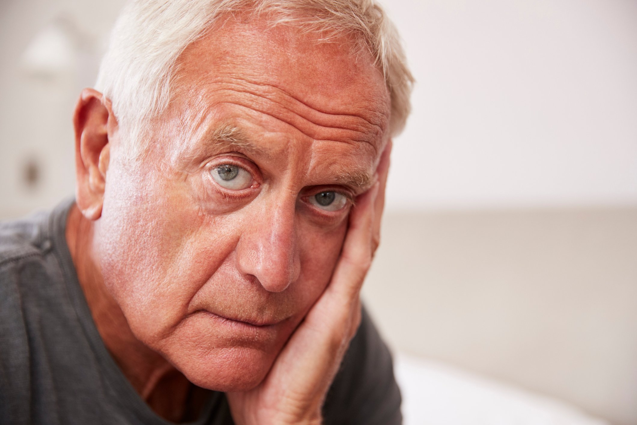 Closeup of older man with serious expression resting face on hand