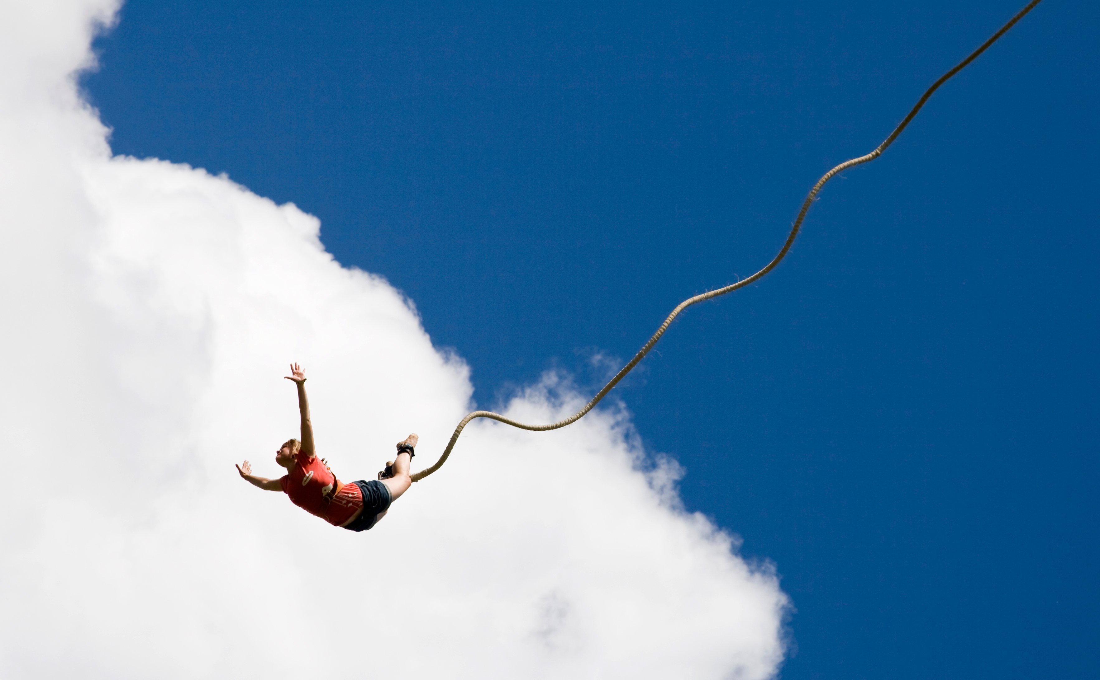 Woman bungee jumping with cloud and blue sky behind her.