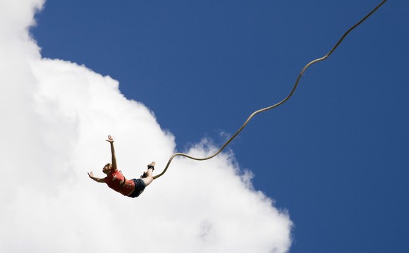 Woman bungee jumping with cloud and blue sky behind her.