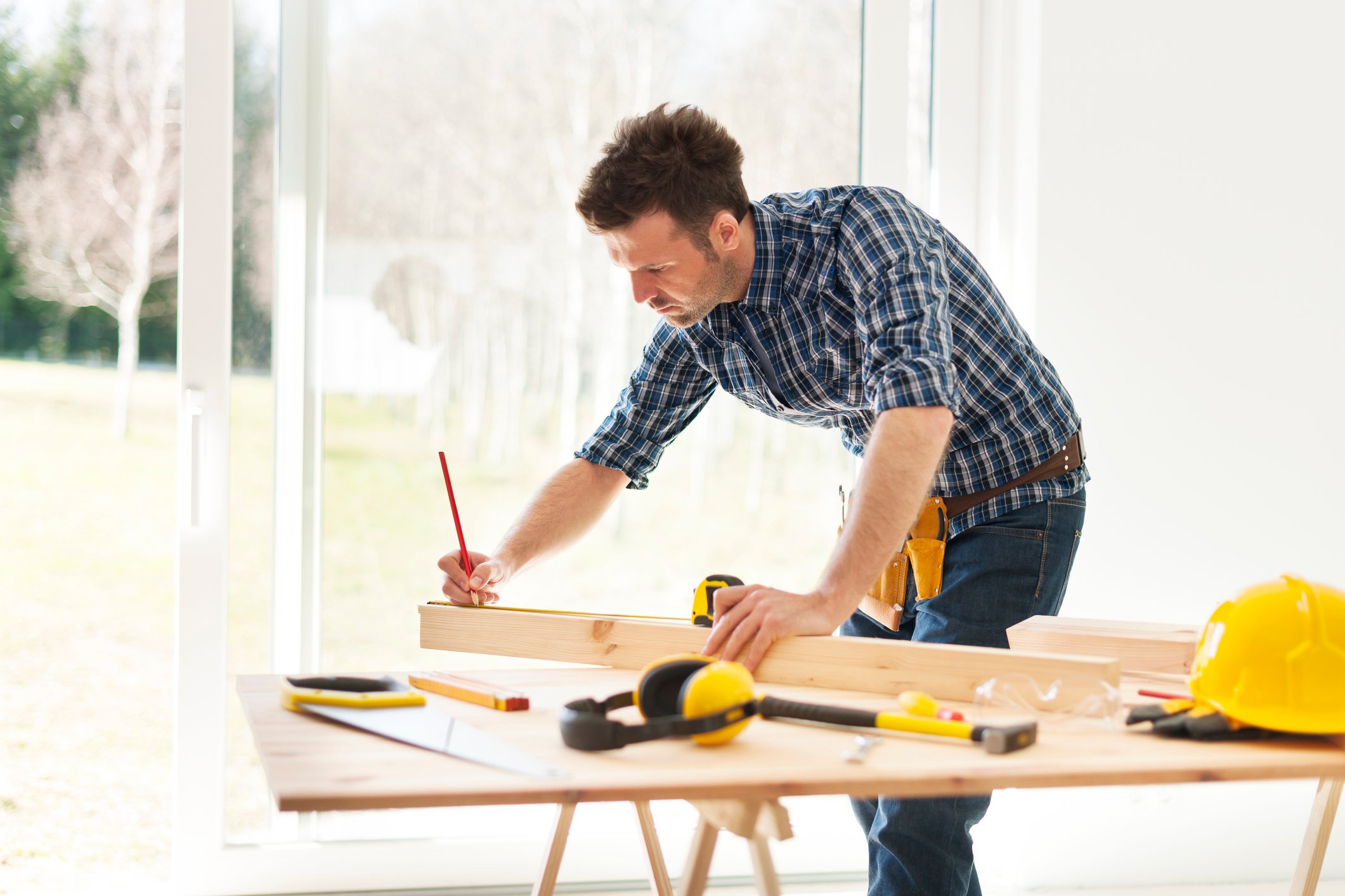 A man working on a drafting table with a yellow construction hat nearby.