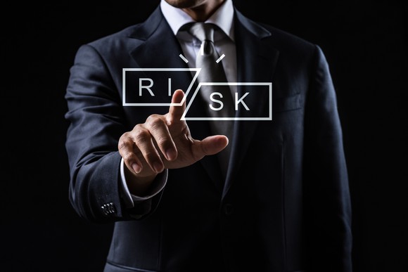 A person in a business suit reaches out and touches the word Risk, which has been cut in two.