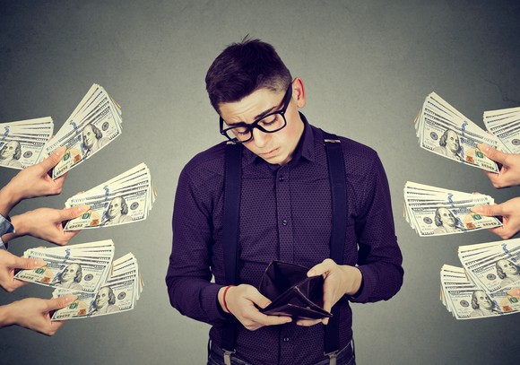 A young man looks at an empty wallet, surrounded by many hands holding cash bundles.