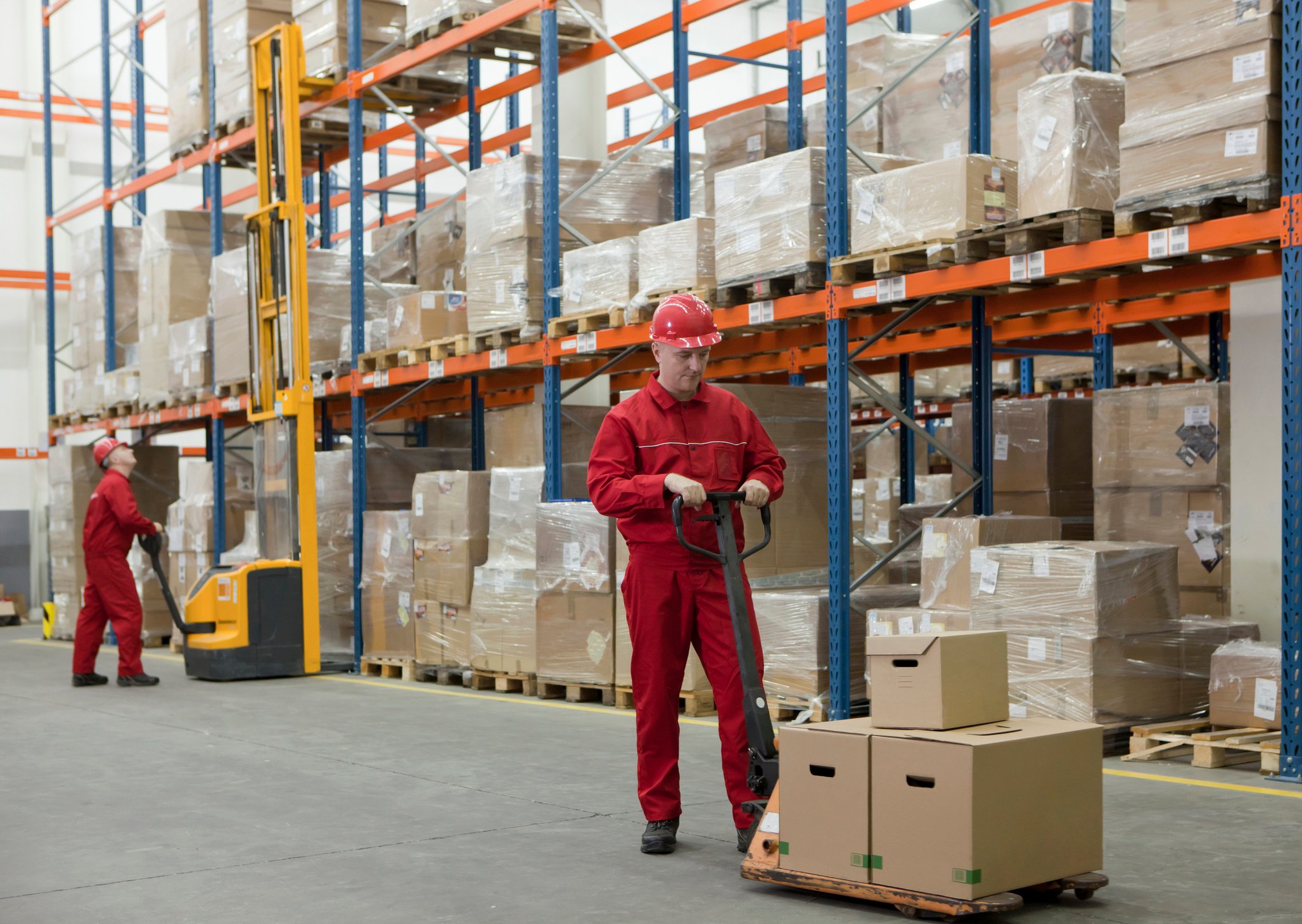 Two workers in a warehouse aisle with machines.