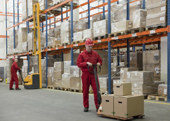 Two workers in a warehouse aisle with machines.