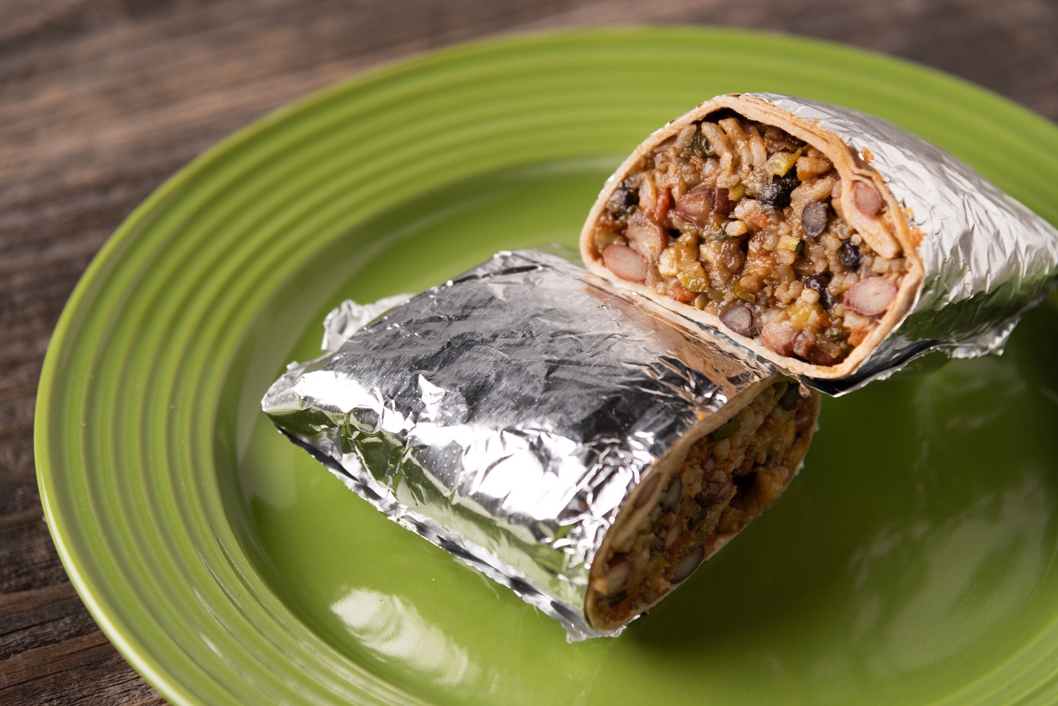 A foil-wrapped burrito is cut in half on a green plate