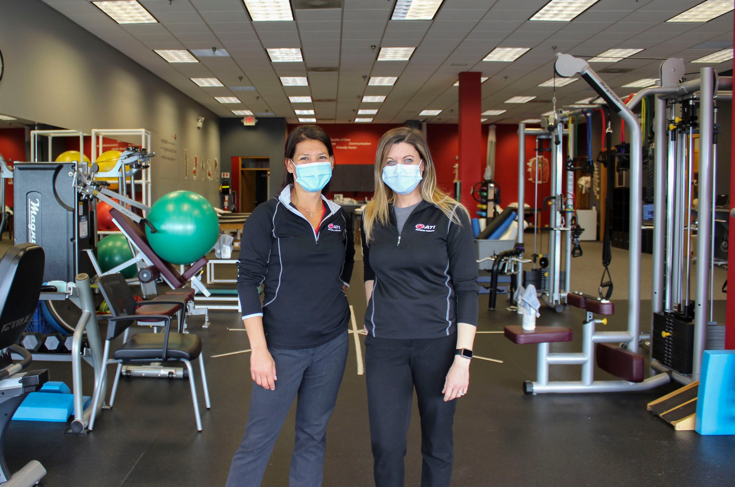 Two workers standing in a room full of exercise equipment. 
