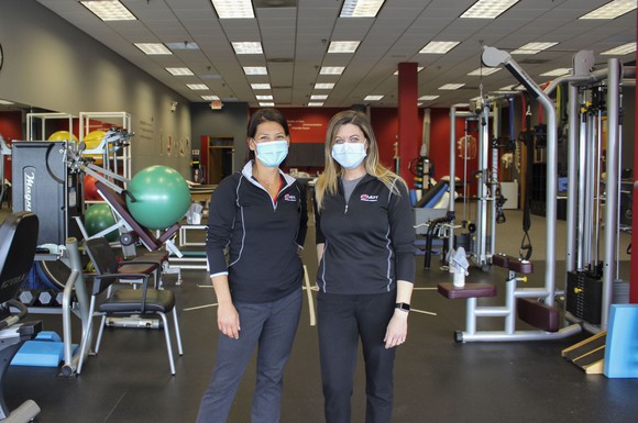 Two workers standing in a room full of exercise equipment. 
