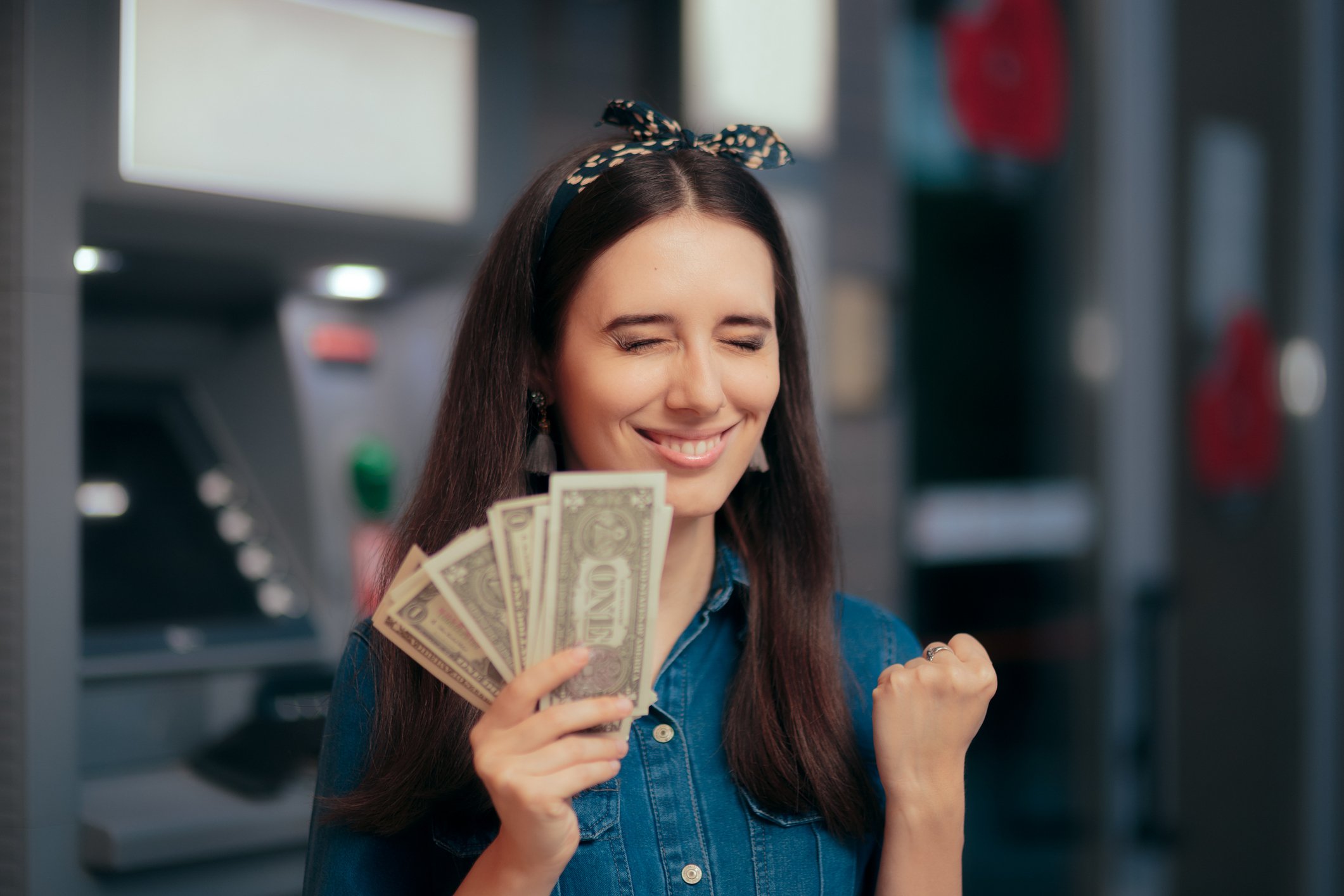Smiling woman clutching money in front of ATMs.