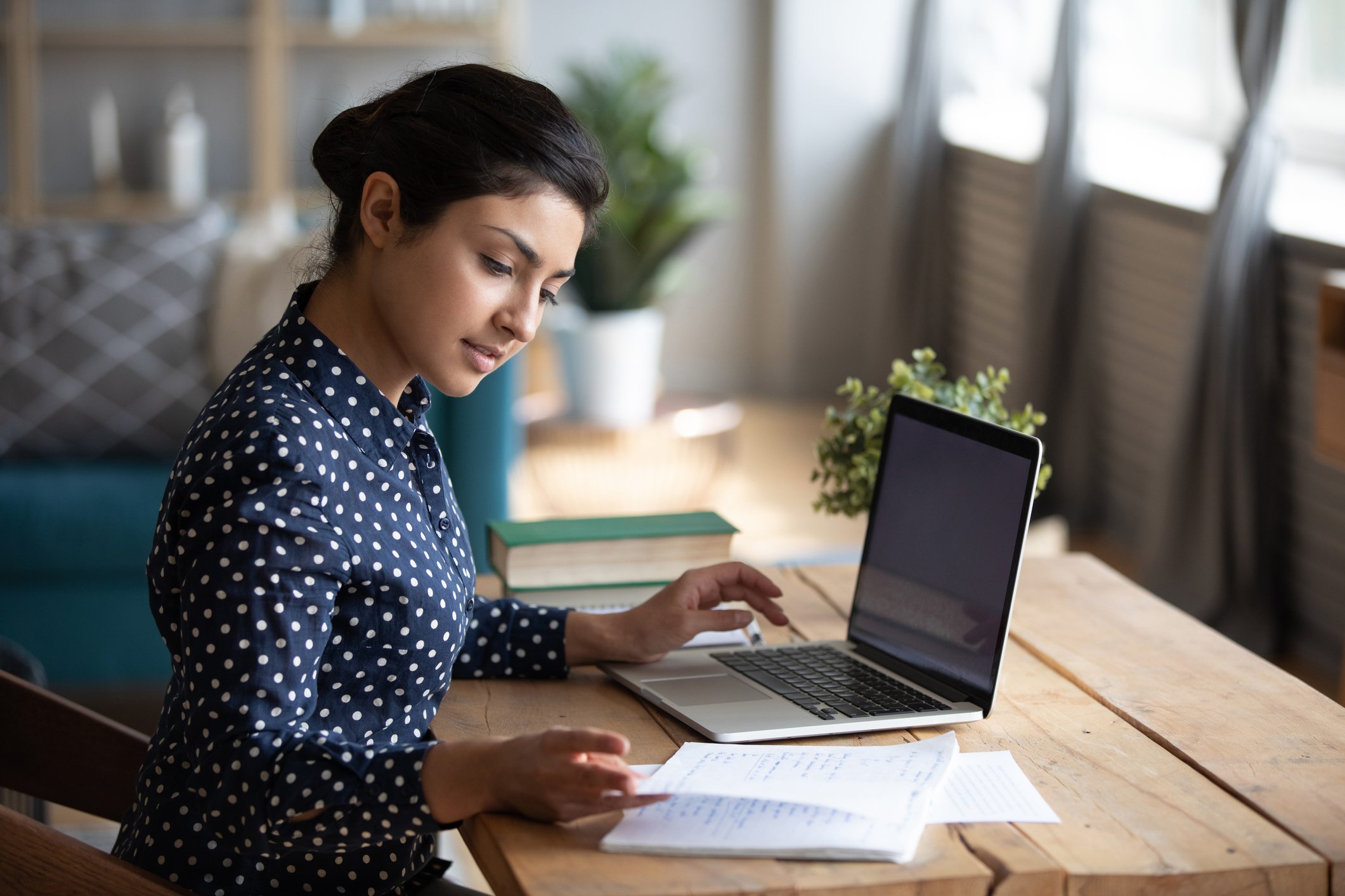 A woman glances as notes as she sits in front of her laptop.