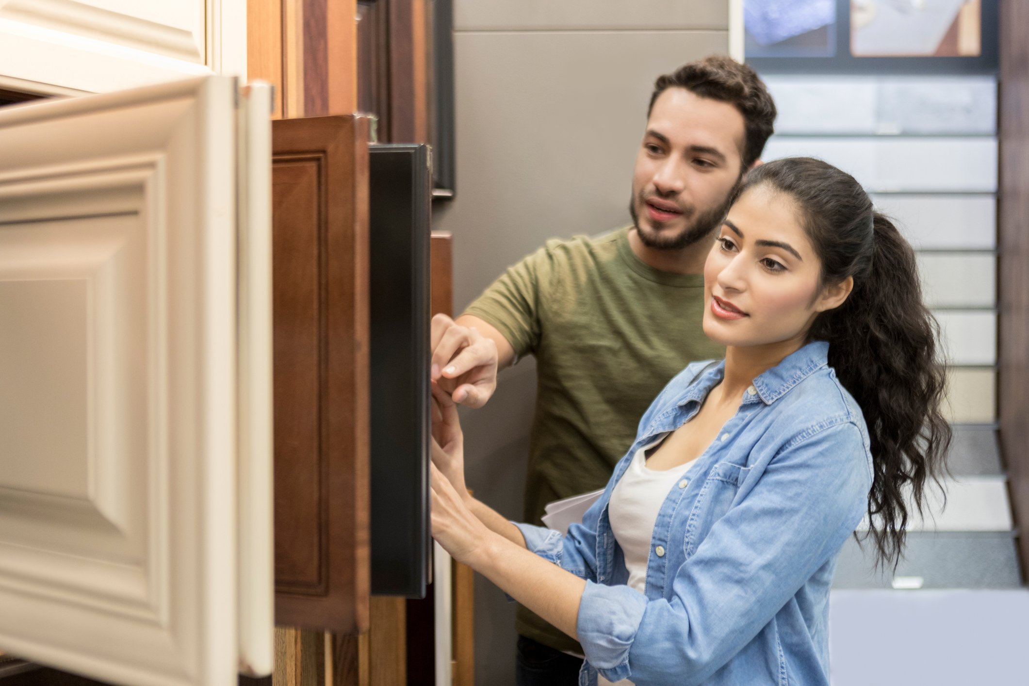 A man and a woman looking at cabinet doors in a store.