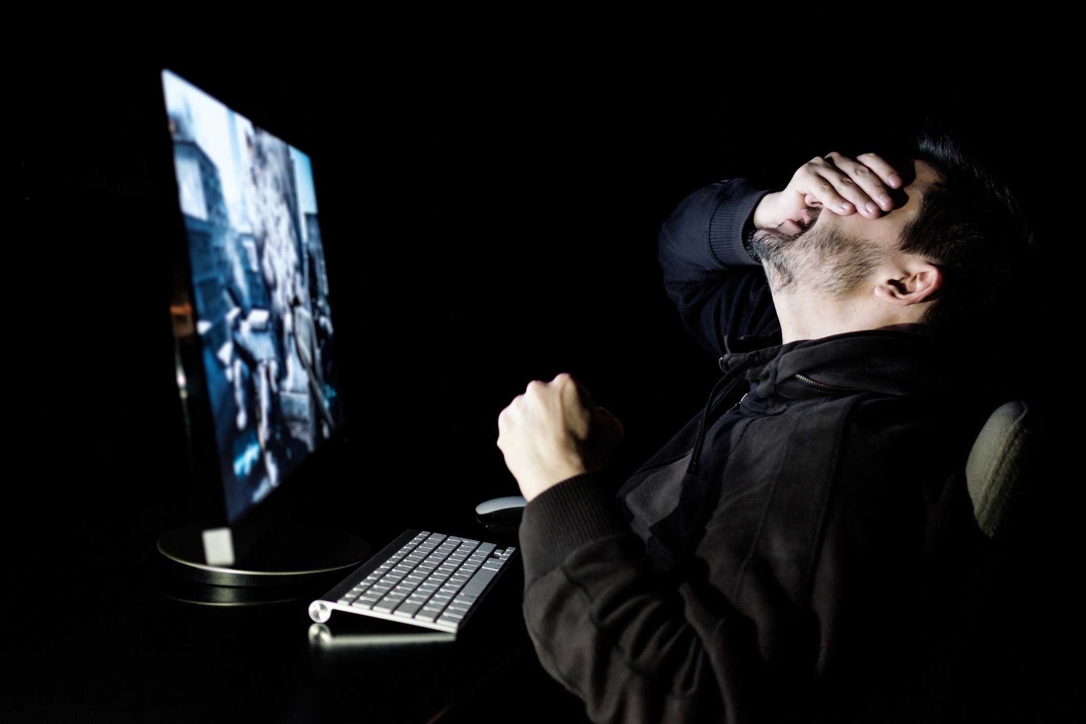 A person playing a game at his computer puts his hand over his eyes