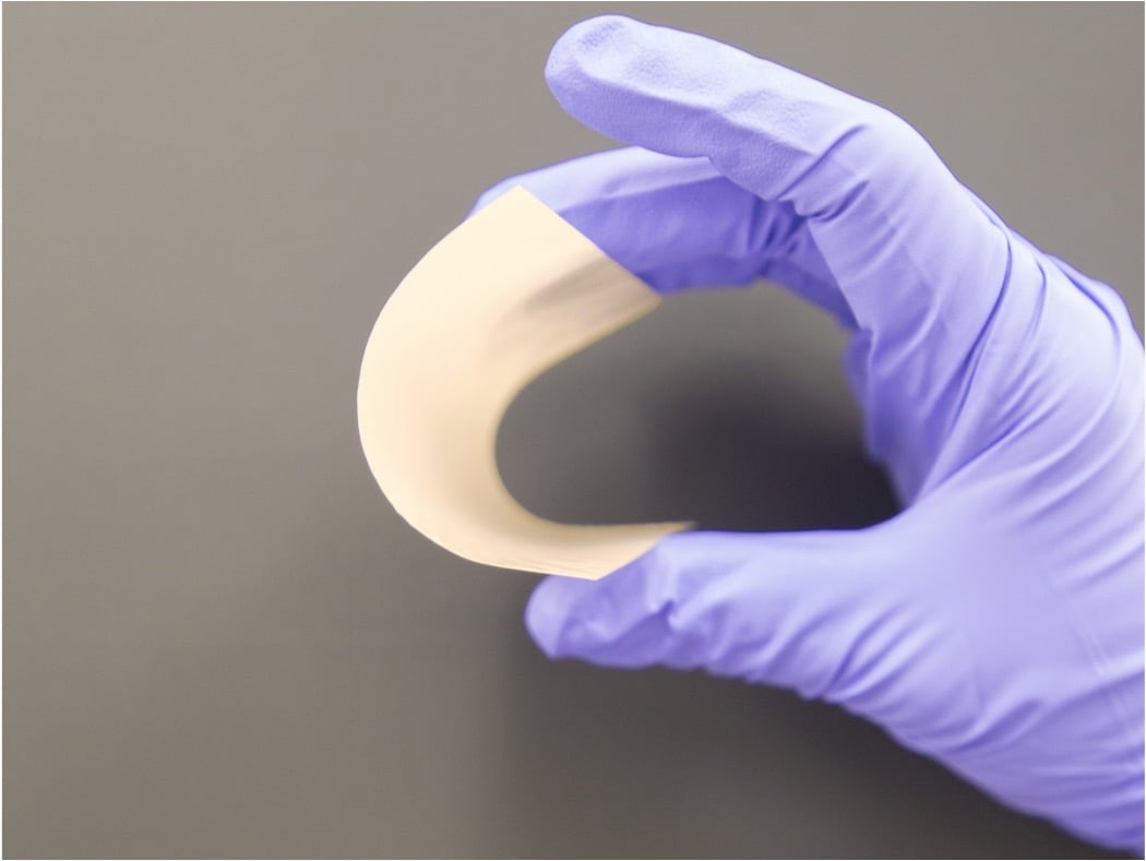 A gloved hand holding a thin ceramic sheet, bent into an arc. 