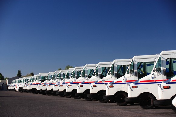 Stock photo of a fleet of U.S. postal service vehicles parked in a line.
