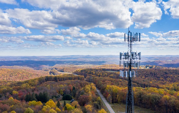 A telecom tower perched above a highway in a hilly, forested, rural area.
