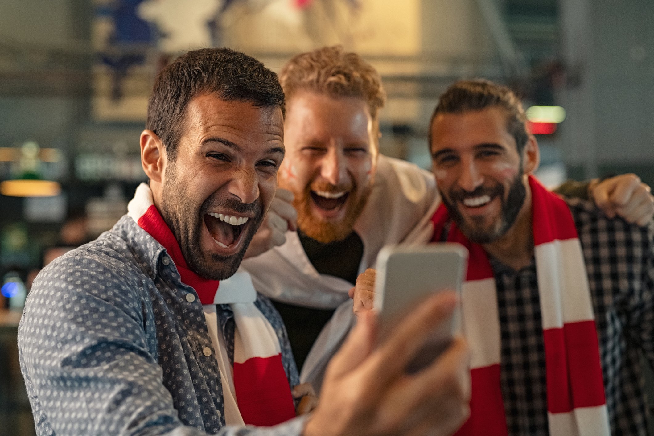 Three friends looking at a phone screen while smiling and cheering