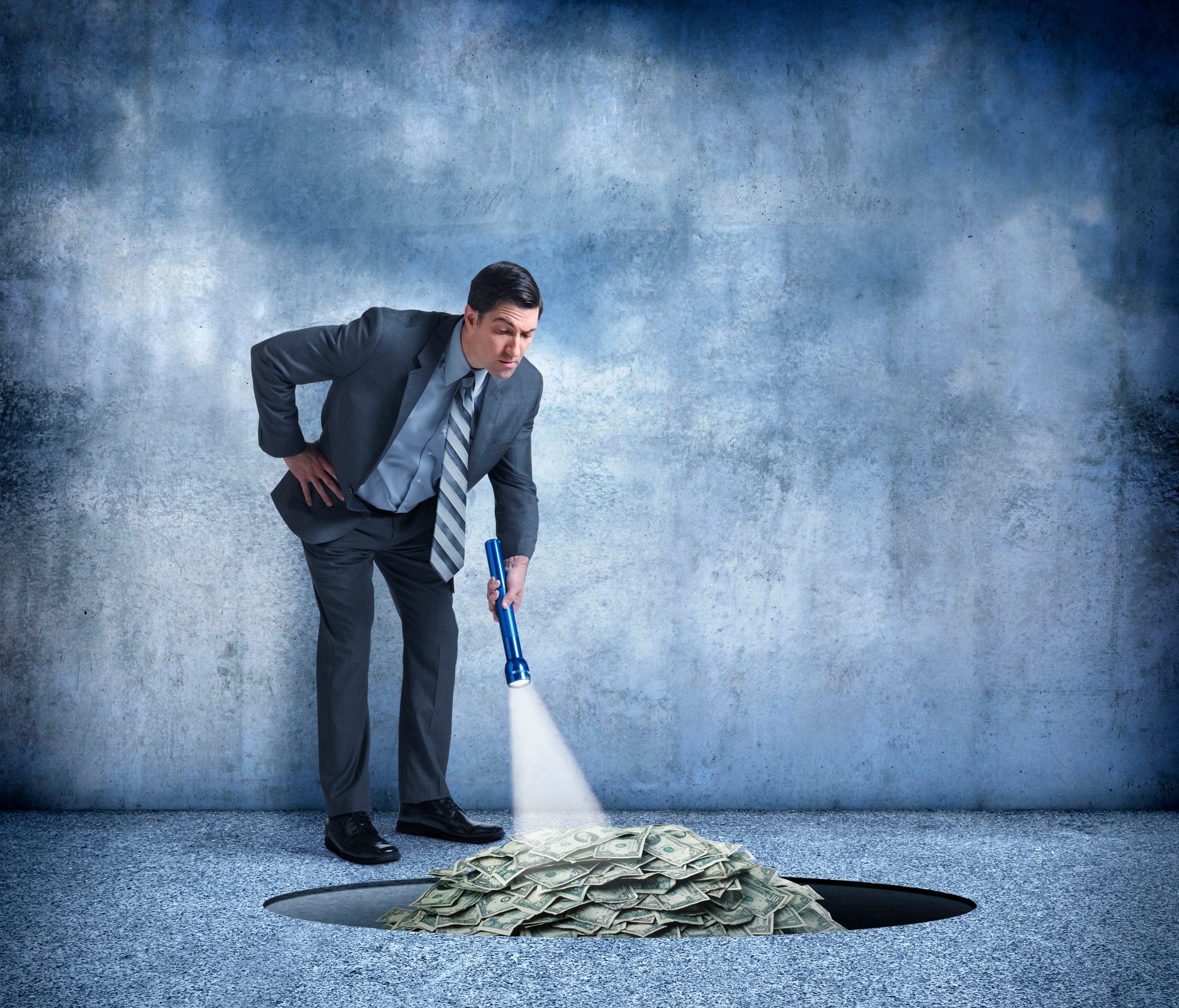 Man in suit shining flashlight on hole filled with cash