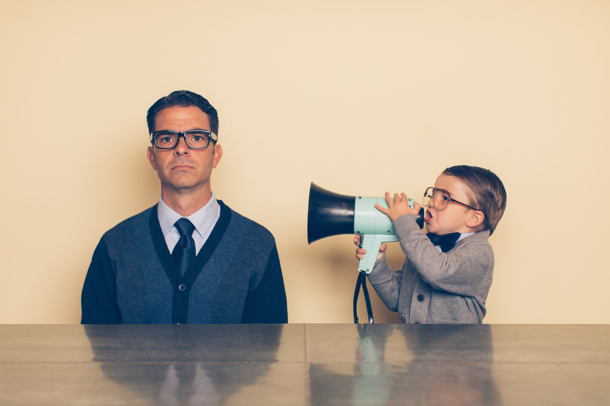 A child uses a megaphone to talk to a man who is sitting, seemingly not paying attention
