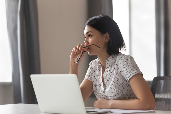 A woman at a laptop, deep in thought, making a decision.